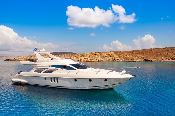 White yacht sailing in clear blue sea near rocky shore