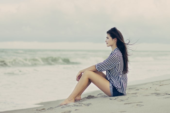 Brunette girl sitting on a sandy beach by the sea