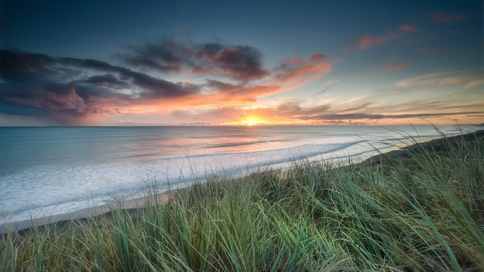 Sunset over the ocean with grass in the foreground