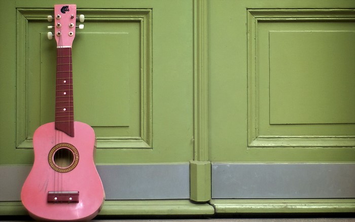 Pink ukulele leaning against a green door