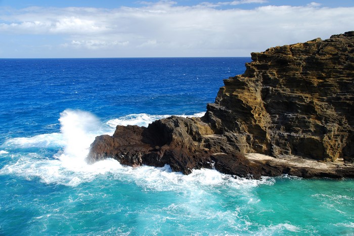 Ocean waves crashing on rocky cliffs under a blue sky