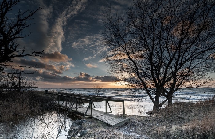 Wooden bridge over water near sea at sunset