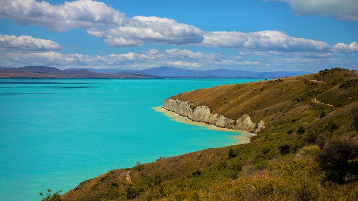 Turquoise lake and rolling hills under a cloudy sky