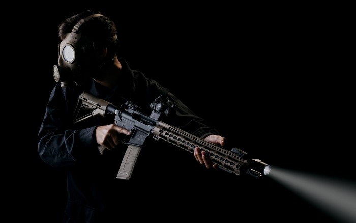 Person in gas mask holding assault rifle with flashlight