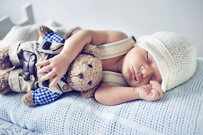 Infant sleeping with teddy bear and winter hat