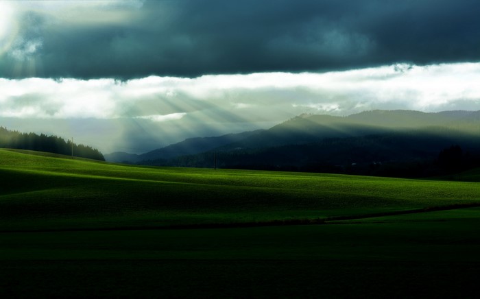Sunbeams through clouds over rolling green fields and mountains