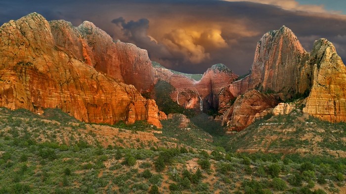 Red rock mountains with waterfalls under a stormy sky