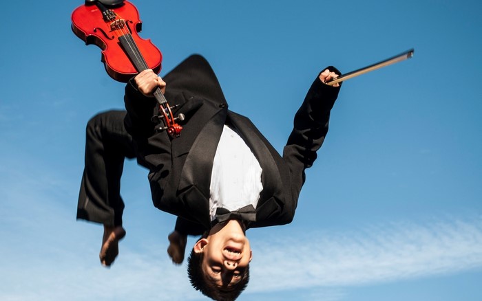 Man in suit doing a backflip with a violin