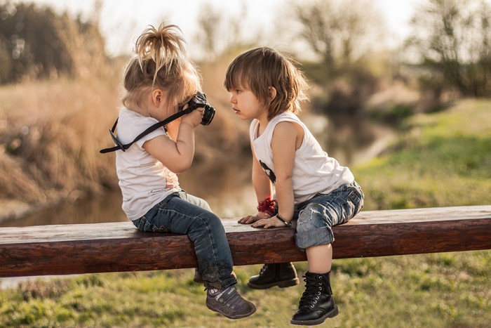 Two children with a camera on a bench