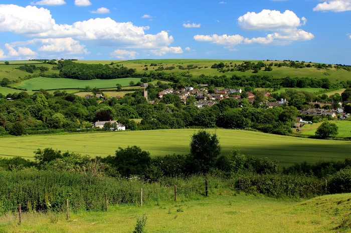 Village in rolling green hills under a blue sky with clouds