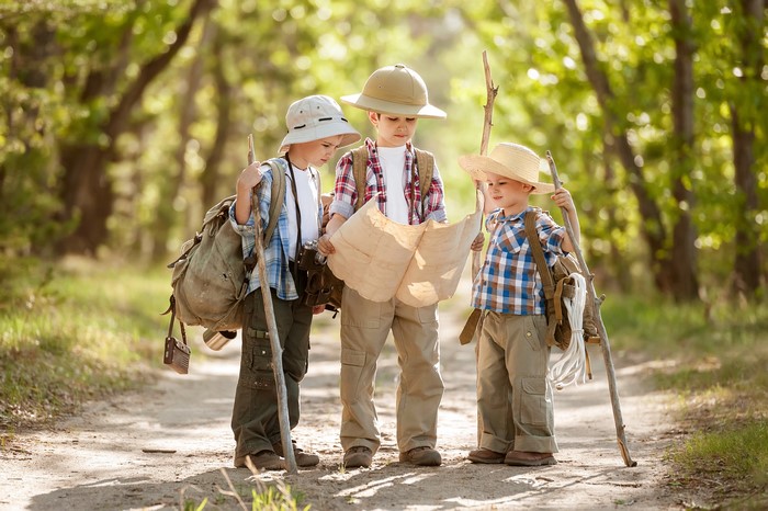 Three boys with backpacks and hats looking at a map in a forest