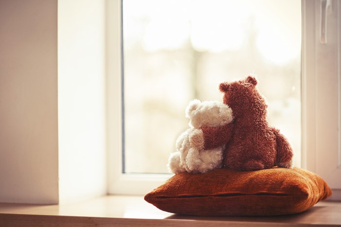 Two teddy bears hugging on a pillow by the window