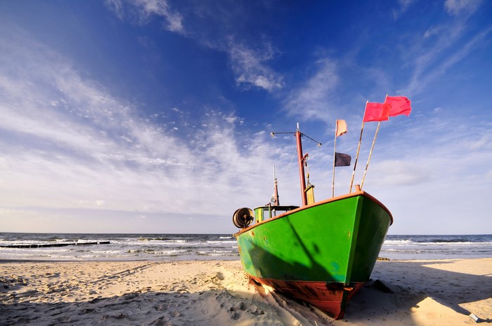 Green fishing boat on a sandy beach with flags