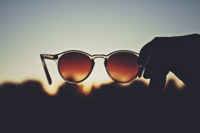Hand holding sunglasses against sunset sky