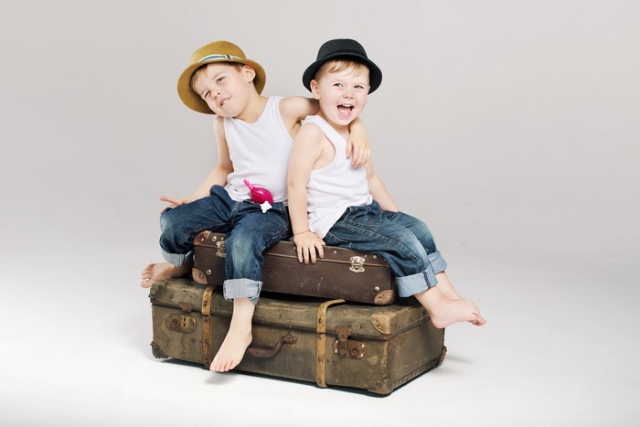 Two Boys in Hats Sitting on Suitcases
