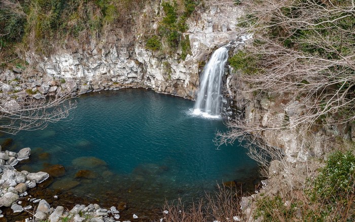 Waterfall cascading into a blue pool surrounded by rocks and trees