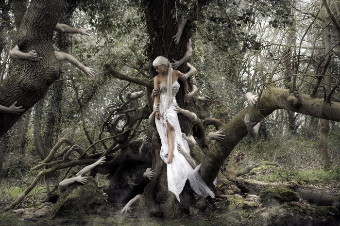 Woman in white dress surrounded by hands in a forest