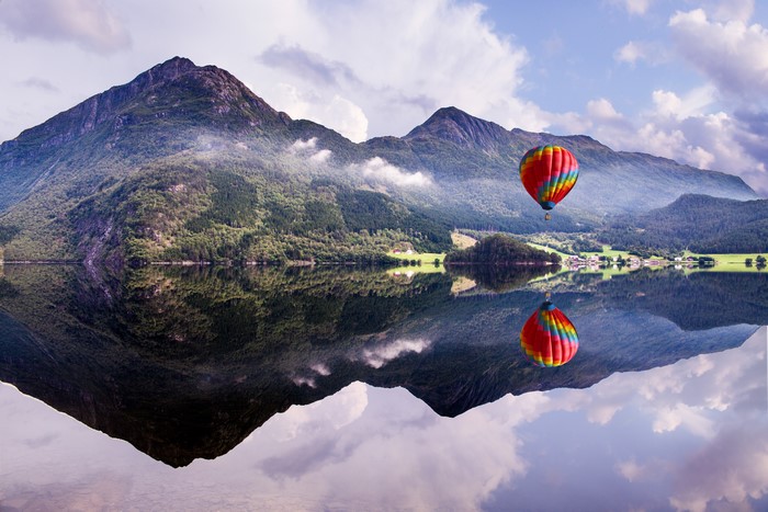 Hot air balloon over mountains and lake reflection
