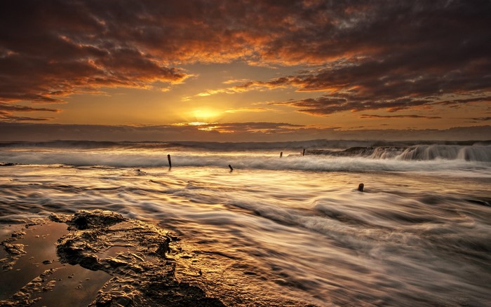 Sunset over the ocean with waves and wooden posts