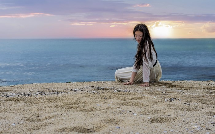 Girl sitting on a beach at sunset