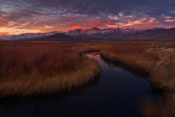 River flowing through marshland with mountains at sunset