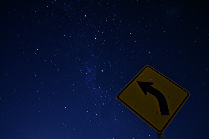 Road sign with arrow against starry night sky