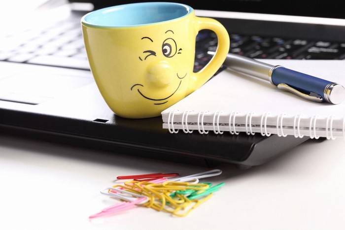 Yellow smiley mug on a laptop with pen and notebook