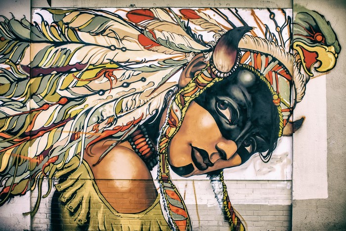 Graffiti of a woman with a war bonnet and mask