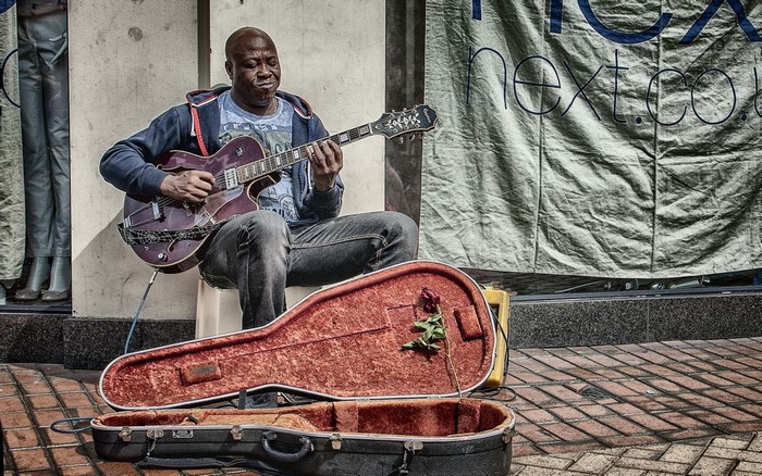 Man playing guitar on street with guitar case