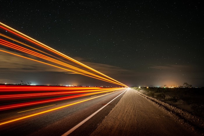 Light trails on a highway at night under a starry sky