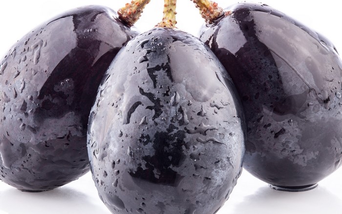 Three dark grapes with water droplets