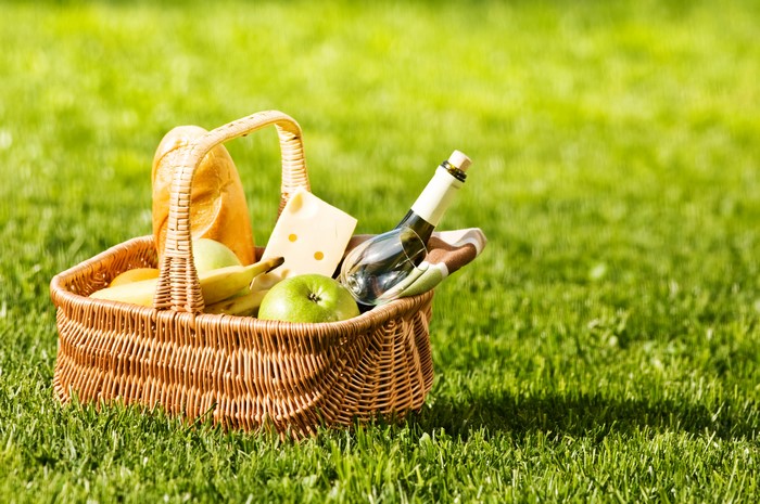 Picnic basket with bread, cheese, fruit, and wine on grass