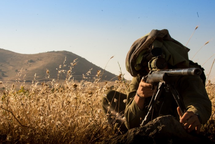 Soldier aiming a sniper rifle in a field