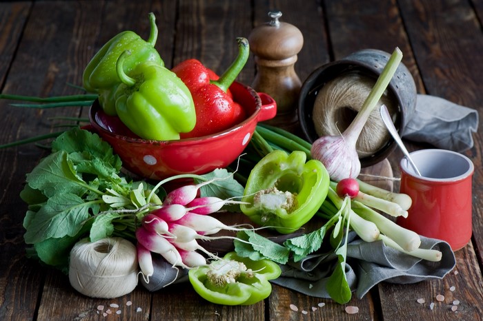 Bell peppers, radishes, garlic, and green onions on a wooden table