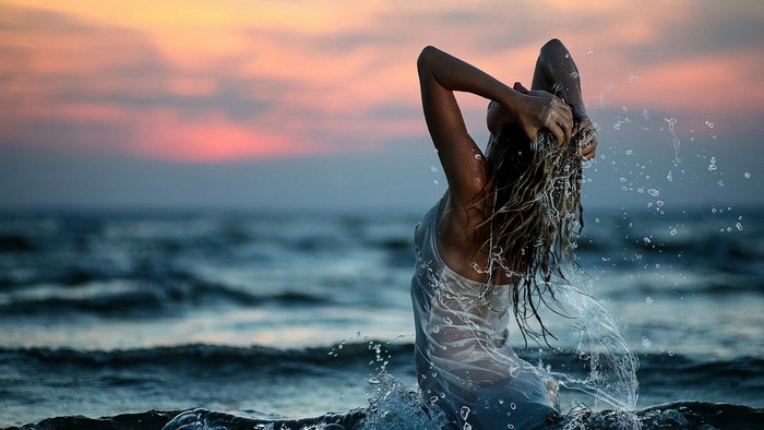 Woman in wet dress splashing in ocean at sunset