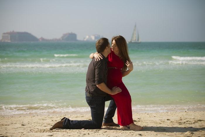 Couple on a beach with buildings and sailboat in background