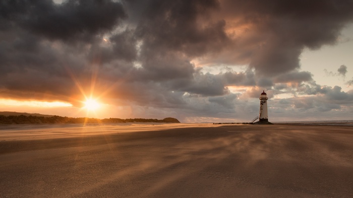 Lighthouse on a beach at sunset with dramatic clouds
