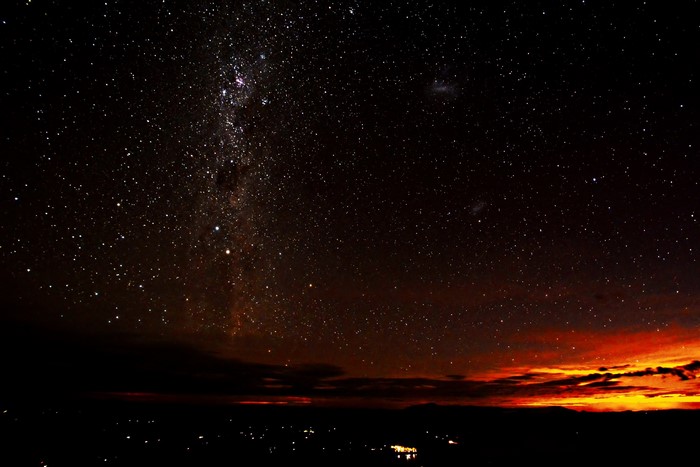 Milky Way galaxy over a dark landscape with city lights