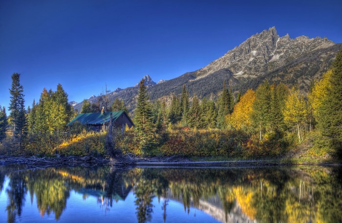 Cabin by a lake with mountains and autumn trees