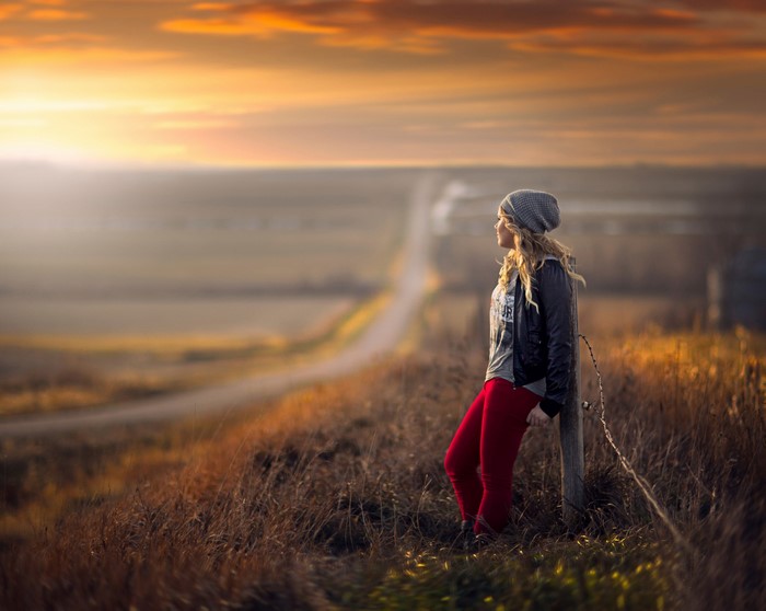 Girl in winter hat and red pants looking at sunset