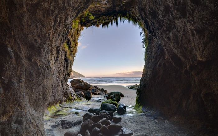 Cave entrance overlooking a beach and ocean at sunset
