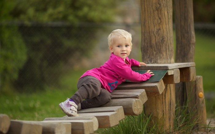 Blonde toddler girl climbing on wooden playground equipment