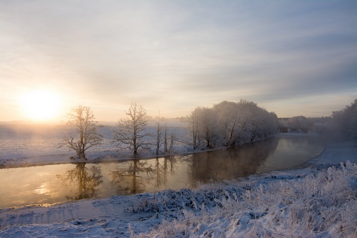 Winter sunrise over a frozen river with trees