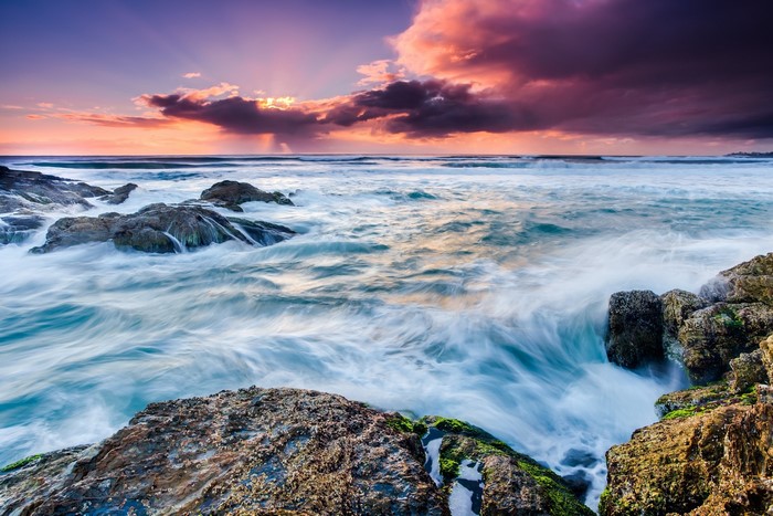 Ocean waves crashing on rocky shore at sunset