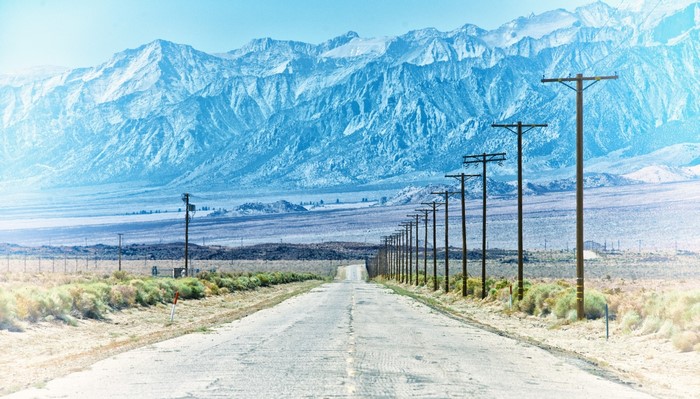 Road leading to snow-capped mountains with utility poles