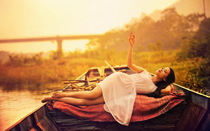 Asian woman in white dress lying in a boat