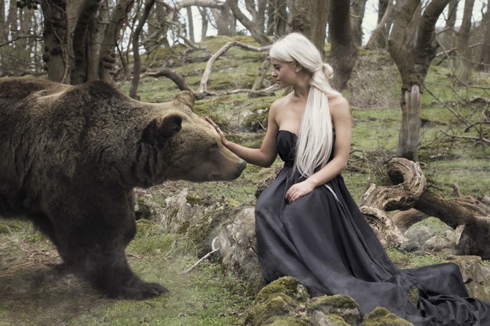 Woman in black dress petting a brown bear in a forest