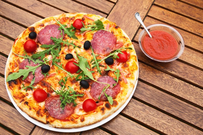 Pizza with sausage, tomatoes, olives, and arugula