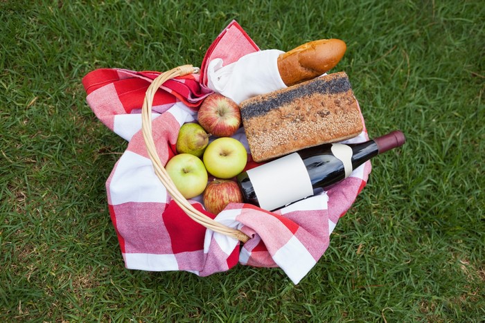 Picnic basket with wine, apples, and bread on grass