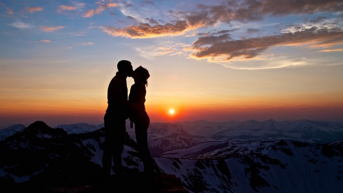 Couple kissing on mountain peak at sunset